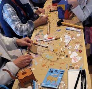 板猫屋ワークショップにて、子供からお年寄りまで3世代で一緒に板猫の色塗りを楽しんでいる様子